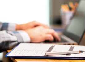 Image of someone working on laptop, hands and forearms in a shirt only visible