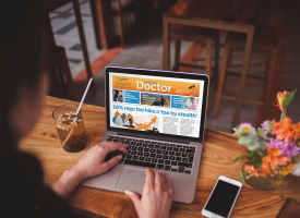 ID: Close up of a laptop sitting on a bench in a cafe or kitchen. The latest issue of Canberra Doctor is on the screen.